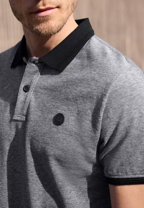 Homme porte un polo gris à col et manches noirs, logo rond sur la poitrine.