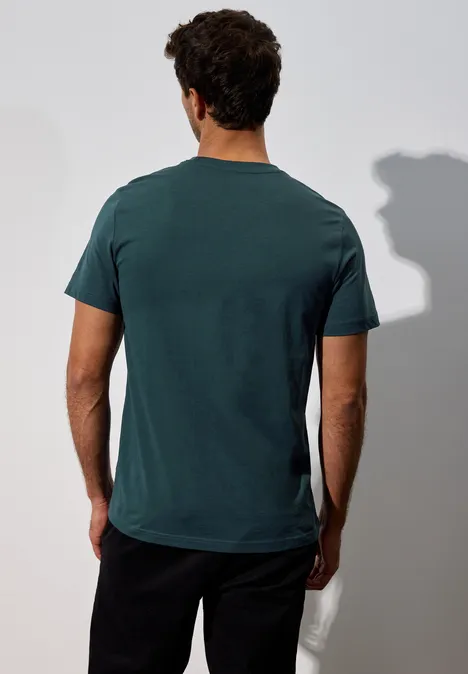Ein Mann steht mit dem Rücken zur Kamera und trägt ein dunkelgrünes T-Shirt.