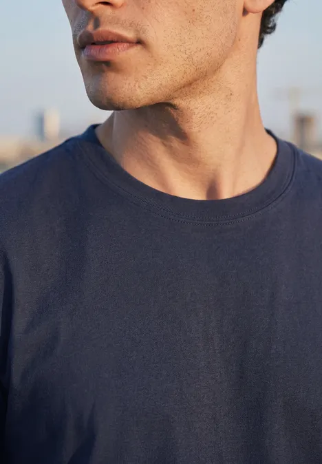 Basic Shirt in effen kleur eclipse blue Nahaufnahme eines Mannes in marineblauem T-Shirt, nur Hals, Kinn und Oberkörper zu sehen.