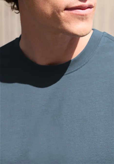 Teilansicht eines Mannes mit blauem T-Shirt, Hals und Kinn vor hellem Hintergrund