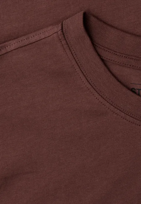 Nahaufnahme eines braunen T-Shirts mit Rundhalsausschnitt und sichtbaren Nähten.