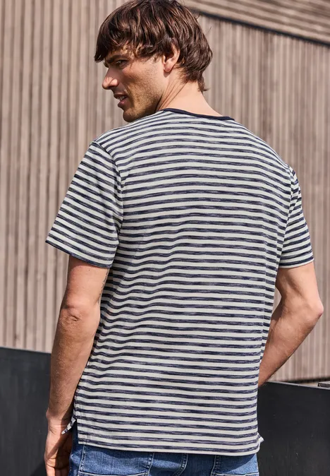 Ein Mann von hinten in gestreiftem T-Shirt vor einer Holzfassade.