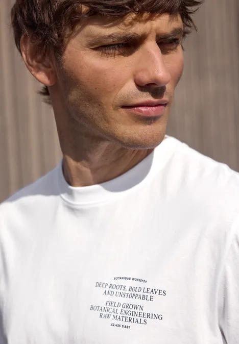 Porträt eines Mannes in weißem T-Shirt mit Text vor Holzwand.