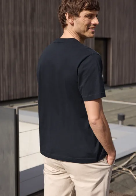 Ein Mann von hinten in schwarzem T-Shirt und beiger Hose vor moderner Gebäudefront.