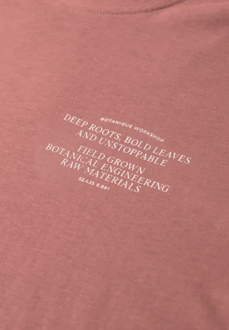 Rosa T-Shirt mit weißem Slogan über tiefe Wurzeln, starke Blätter und nachhaltige Materialien.
