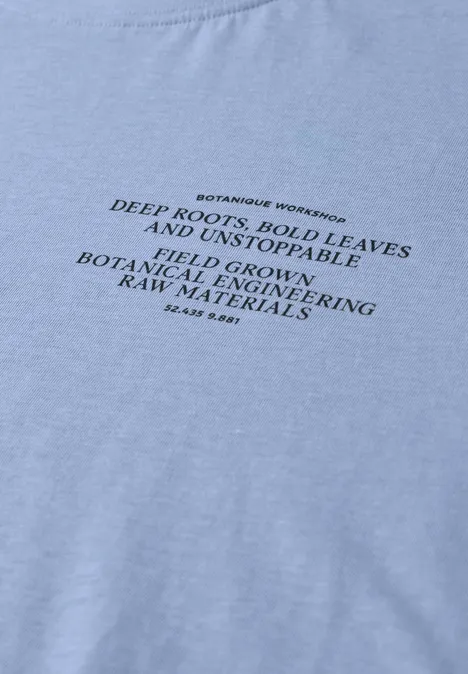 Hellblaues T-Shirt mit schwarzem gedrucktem botanischen Slogan über Wurzeln und Blättern.