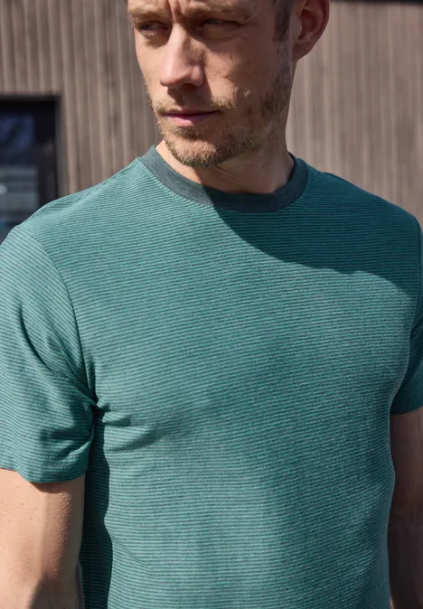 Ein verschwommener Mann in grünem T-Shirt vor Holzwand.