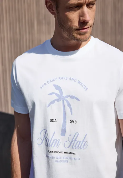 Een man draagt een wit t-shirt met blauwe palmprint en tekst voor een houten achtergrond.