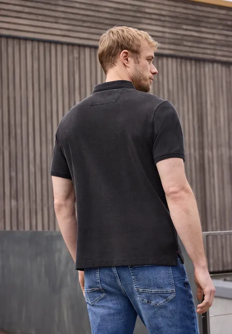 Un homme de dos en T-shirt noir et jean devant un mur en bois