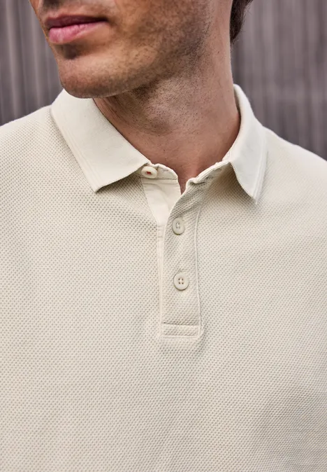 Nahaufnahme eines Mannes in hellbeigem Polo-Shirt, geöffneter Kragen, dezente Struktur