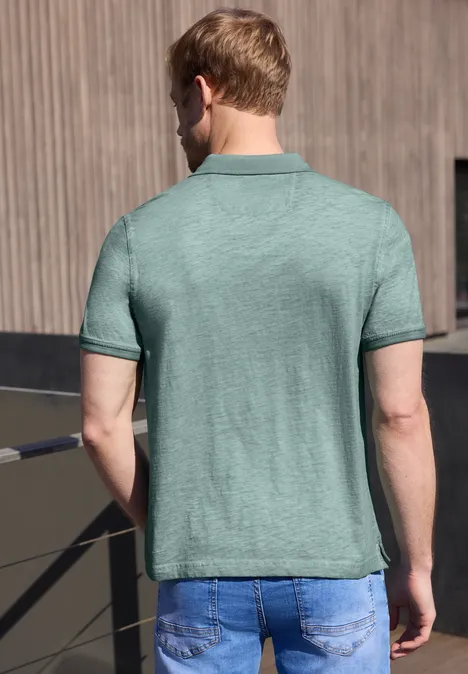 Un homme vu de dos porte un polo vert clair et un jean bleu sur un balcon.