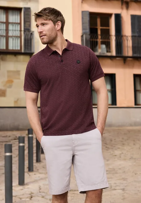 Een man in een bordeaux polo en grijze shorts staat voor een historisch gebouw.