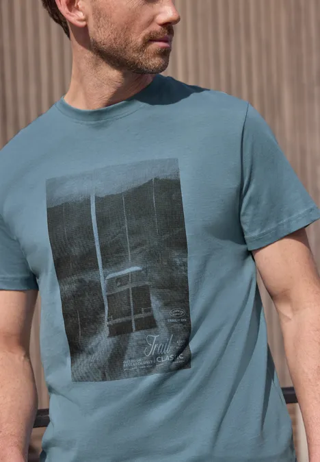Seitlich abgebildeter Mann im türkisfarbenen T-Shirt mit schwarzem Rechteck-Print.