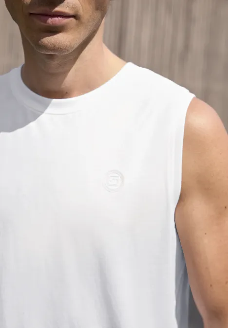 Close-up van een man met een wit mouwloos shirt voor een houten wand.