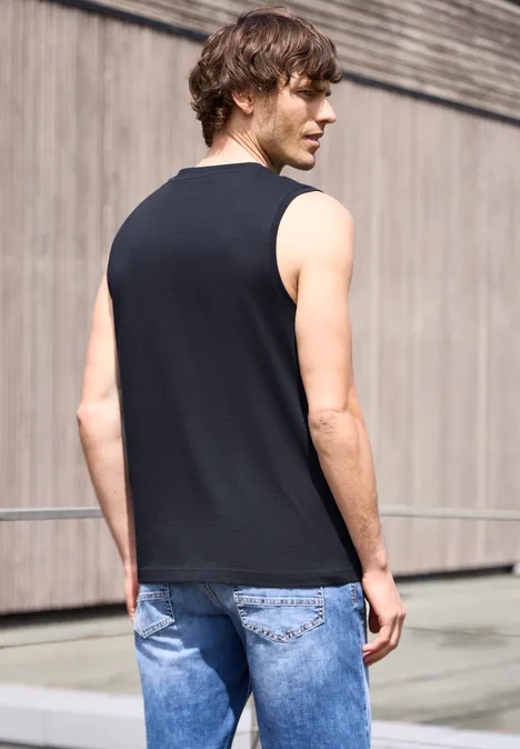 Man van achteren gezien in een zwart mouwloos shirt en blauwe spijkerbroek voor een modern gebouw.