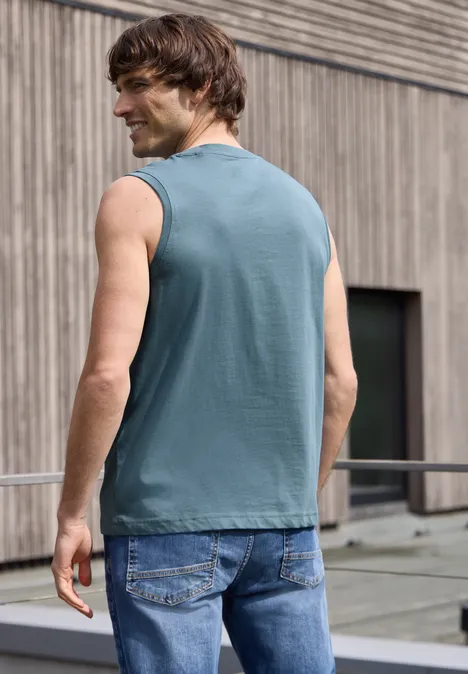 Achteraanzicht van een man in mouwloos shirt en spijkerbroek op een dakbalkon voor een houten gevel.