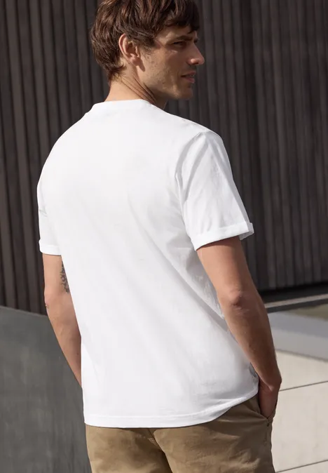 Man van achteren met wit T-shirt en bruine broek voor een houten wand.