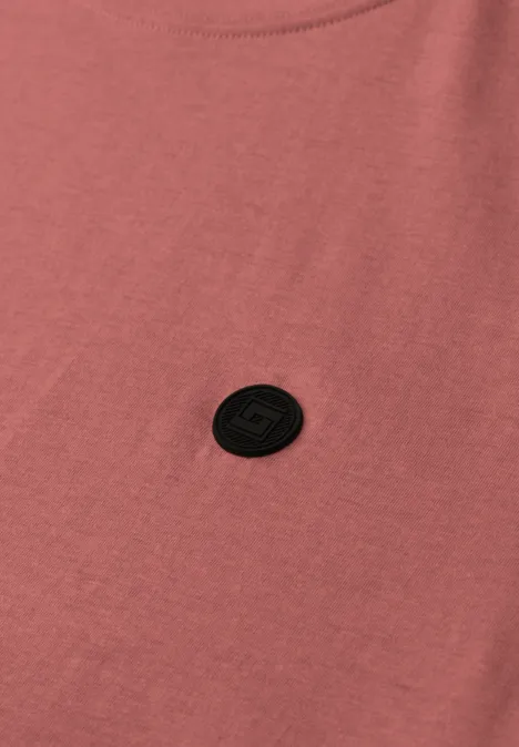Roze T-shirt met een ronde zwarte logo-patch op de borst.