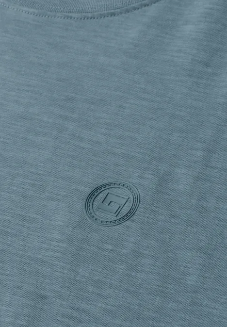 Nahaufnahme eines hellgrünen T-Shirts mit dezentem, rundem Logoaufdruck auf der Brust.