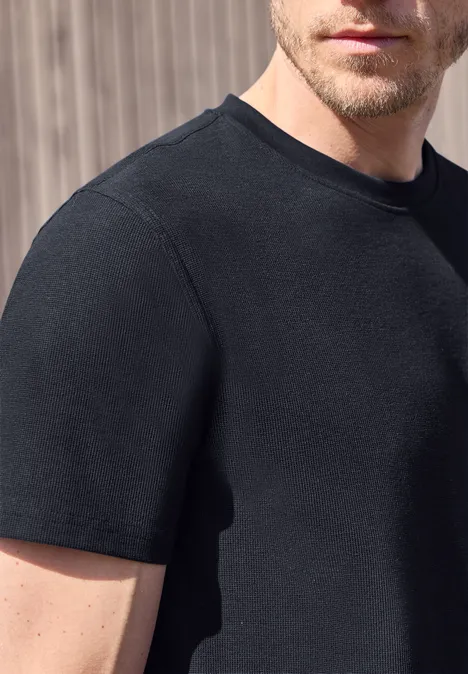 Een man draagt een zwart t-shirt voor een lichte achtergrond.