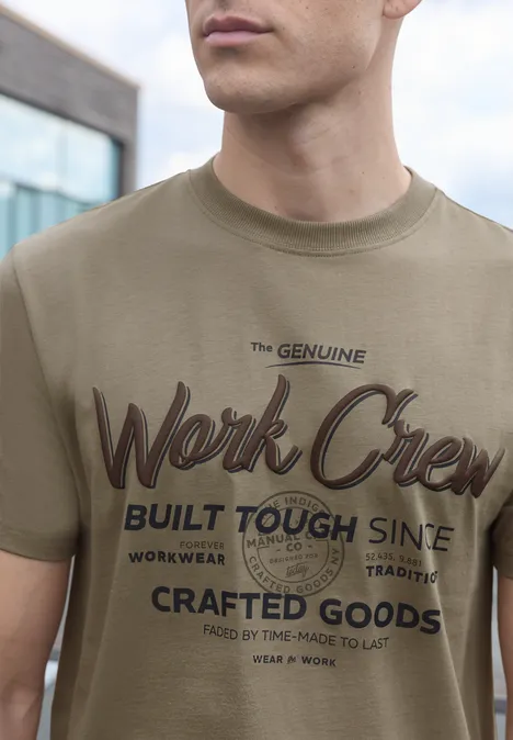 Mann in olivgrünem T-Shirt mit Aufschrift „The Genuine Work Crew Built Tough Since… Crafted Goods“.