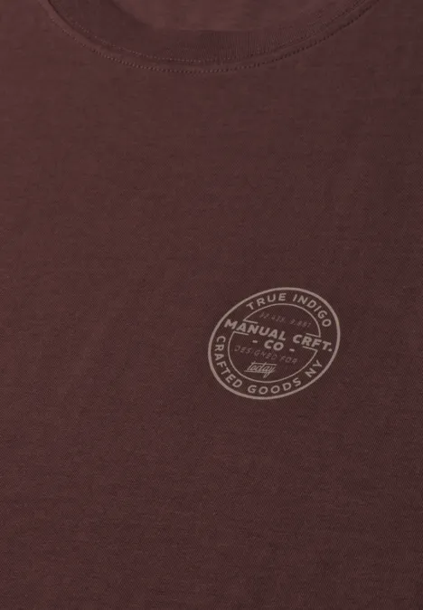 Ein braunes T-Shirt mit rundem Emblem auf der Brust.