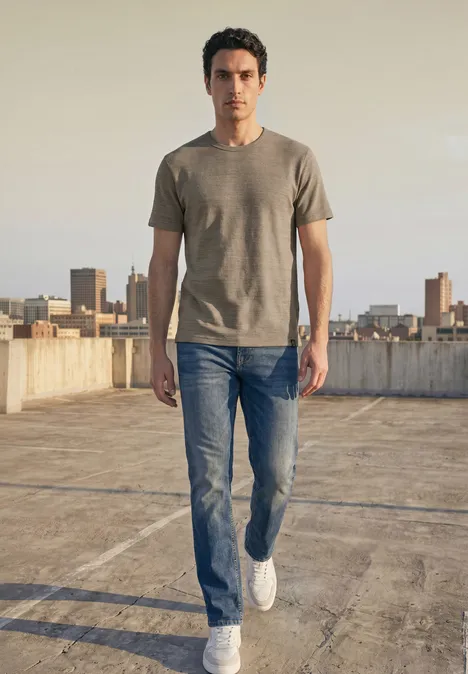 Ein Mann in Jeans und T-Shirt läuft auf einem Dach mit Stadt im Hintergrund.