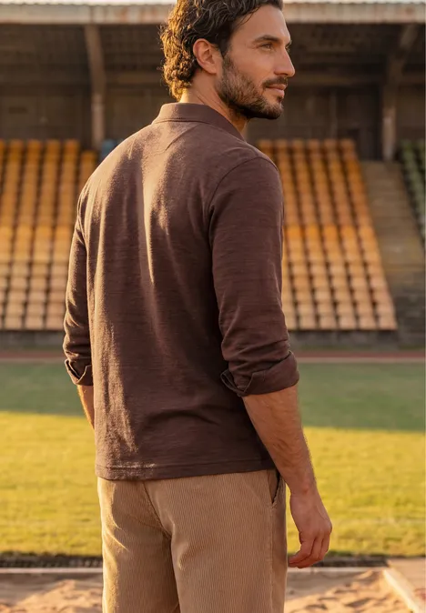 Ein Mann im braunen Outfit steht auf der Sportanlage vor leeren Tribünen und blickt über die Schulter.