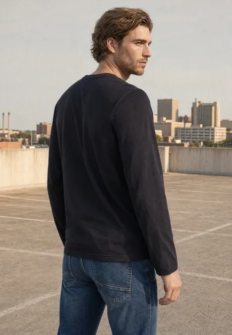Langarm Shirt mit Rundhals in Unifarbe basic black Ein Mann mit schwarzem Langarmshirt und Jeans steht auf einem Parkdeck und blickt in die Ferne.