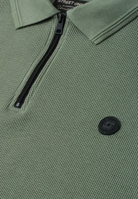 Olivgrünes Polohemd mit Reißverschluss am Kragen und rundem Logo-Patch.