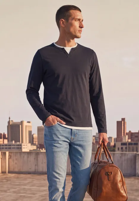 Henleyshirt im 2-in-1-Look dark ink blue Ein Mann steht auf einem Dach mit Stadtblick, trägt Jeans, schwarzen Pullover und hält eine Ledertasche.
