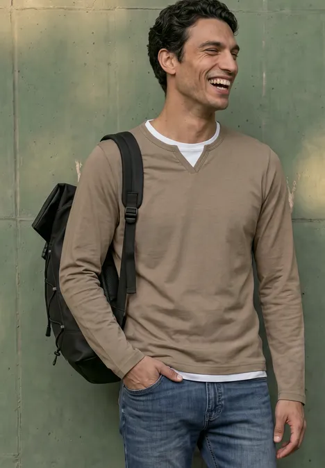 Henleyshirt im 2-in-1-Look antique beige Ein junger Mann mit Rucksack, lächelnd vor einer grünen Wand.