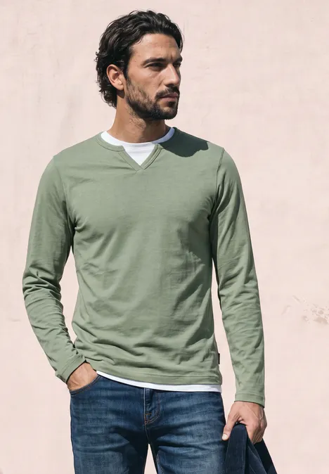 Henleyshirt im 2-in-1-Look willow green Ein Mann in grünem Langarmshirt und Jeans steht vor einer hellen Wand und blickt seitlich.