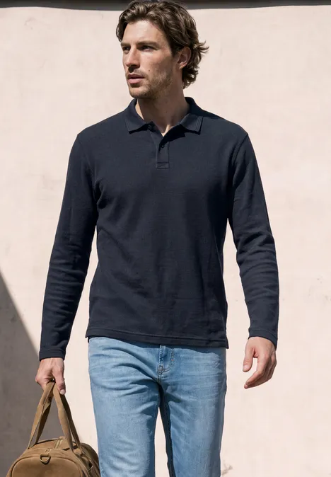 Langarm Poloshirt in Unifarbe dark ink blue Ein Mann trägt ein dunkelblaues Poloshirt, helle Jeans und hält eine braune Ledertasche vor hellem Hintergrund.