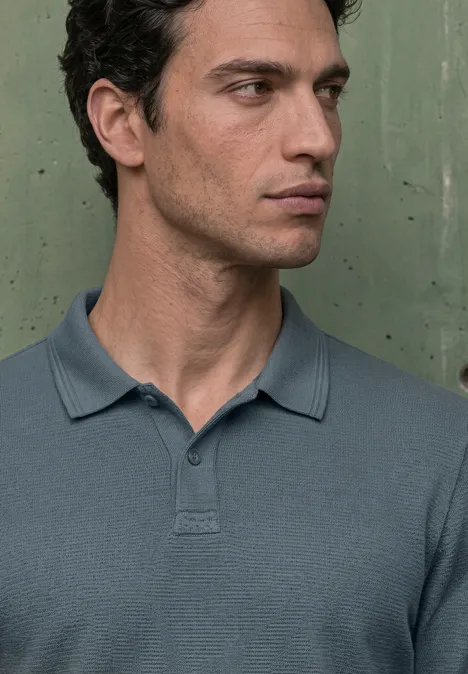 Langarm Poloshirt in Unifarbe vintage blue Ein junger Mann in einem grauen Polohemd vor grünem Hintergrund, Blick nach rechts, neutraler Gesichtsausdruck.