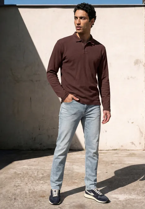 Langarm Poloshirt in Unifarbe maroon brown Ein Mann in braunem Langarm-Poloshirt, hellen Jeans und Sneakern steht an einer sonnigen Wand.