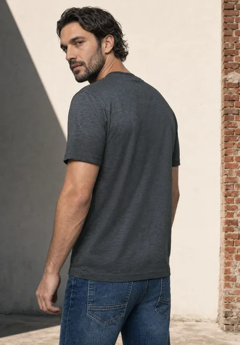 Ein Mann steht seitlich im grauen T-Shirt und blauen Jeans und blickt über die Schulter nach hinten.