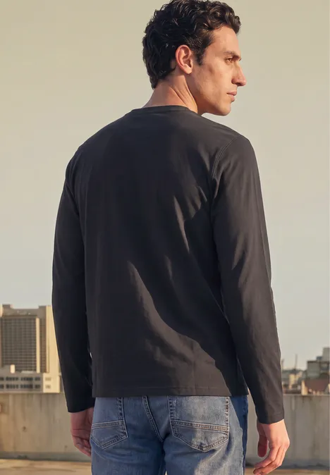Angerautes Henleyshirt mit Printdetail basic black Ein Mann steht seitlich auf einem Dachparkplatz, trägt langärmliges Shirt und Jeans, Blick über die Schulter.