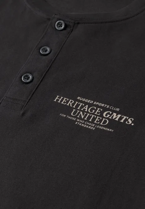 Angerautes Henleyshirt mit Printdetail basic black Schwarzes Shirt mit Knopfleiste und goldfarbenem Schriftzug 'Heritage GMTS UNITED'.