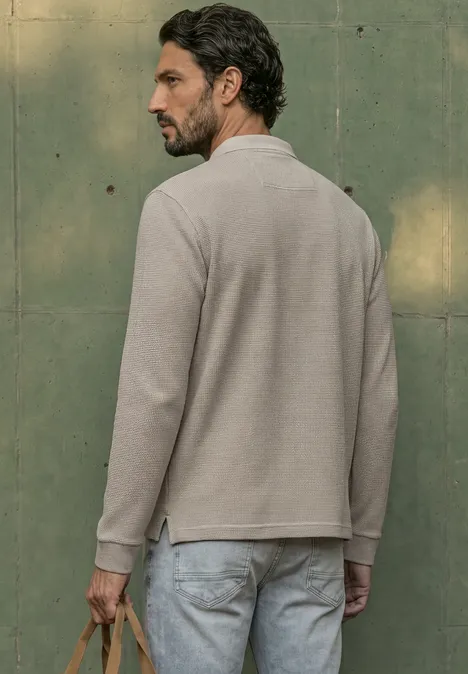 Langarm Poloshirt in Waffelstruktur antique beige Mann im Profil, trägt langärmeliges Polo und Jeans, steht vor einer grünen Wand.