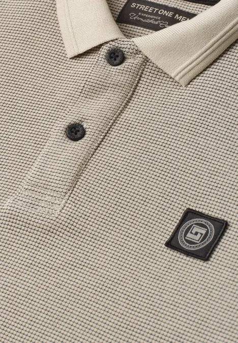 Langarm Poloshirt in Waffelstruktur antique beige Nahaufnahme eines beigen Pikee-Poloshirts mit schwarzem Logo-Patch auf der Brust und zwei Knöpfen.