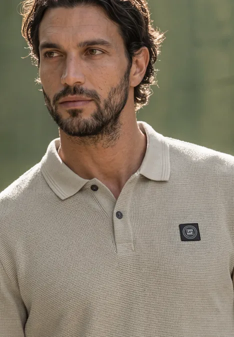 Langarm Poloshirt in Waffelstruktur antique beige Ein Mann mit leichtem Bart trägt ein beiges Poloshirt vor unscharfem Naturhintergrund.