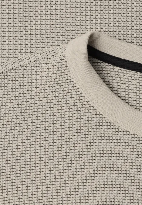 Nahaufnahme eines beigen Strickpullovers mit feinem Waffelmuster und Rundhalsausschnitt.