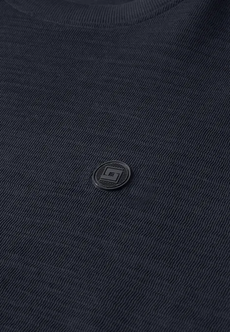 Gros plan d'un tissu noir texturé avec un petit logo rond discret au centre.