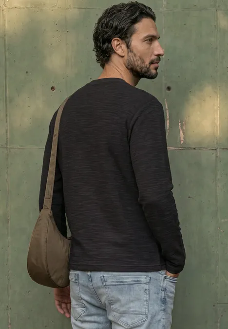Langarm Shirt mit Rundhals in Unifarbe basic black Ein bärtiger Mann in schwarzem Pullover und hellen Jeans trägt eine grüne Schultertasche vor einer grünen Wand.