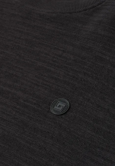 Langarm Shirt mit Rundhals in Unifarbe basic black Nahaufnahme eines schwarzen Strickpullovers mit rundem Ausschnitt und kleinem, rundem Logo-Emblem auf der Brust.