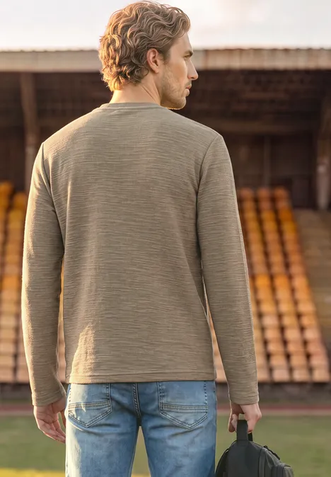 Langarm Shirt mit Rundhals in Unifarbe antique beige Ein Mann steht von hinten vor Tribüne, trägt grünen Pullover, Jeans und hält eine Tasche.