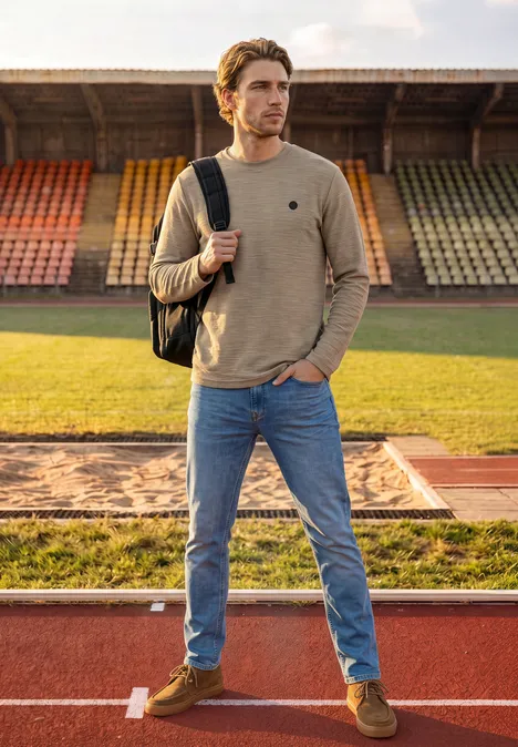 Langarm Shirt mit Rundhals in Unifarbe antique beige Ein junger Mann mit Rucksack steht auf einer Laufbahn vor leeren Tribünen.