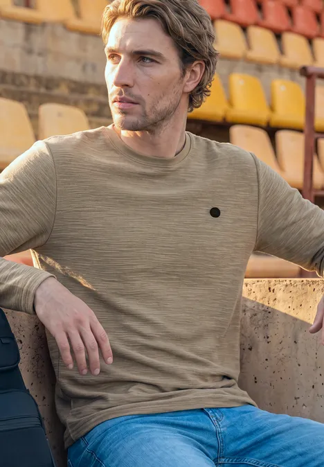 Langarm Shirt mit Rundhals in Unifarbe antique beige Ein Mann in beigem Pullover und Jeans sitzt auf Stadionrängen.