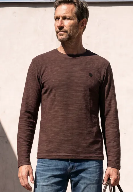 Langarm Shirt mit Rundhals in Unifarbe maroon brown Ein Mann steht vor heller Wand, trägt braunes Langarmshirt, blaue Jeans und hält eine Tasche.